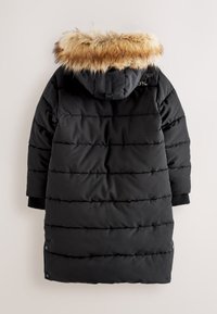 Manteau d’hiver long matelassé noir avec capuche amovible bordée de fausse fourrure beige et blanche, poignets côtelés et boutons-pression le long des côtés.