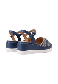 Sandali sintetici blu navy con tomaia in tessuto intrecciato, cinturino alla caviglia regolabile e suola piatta bianca. Superficie testurizzata e design con cinturini incrociati.