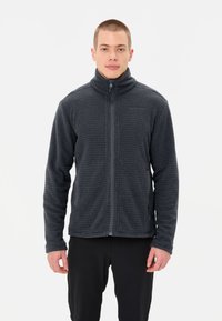 Giacca in fleece grigia con colletto alto, motivo testurizzato, zip frontale e due tasche laterali, indossata sopra pantaloni neri.