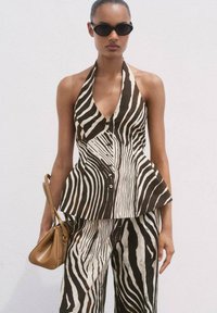 Braun-weißer gestreifter Peplum-Top mit Halsband und Knopfverschluss, kombiniert mit passenden Schlaghosen. Braune Handtasche und dunkle Sonnenbrille.