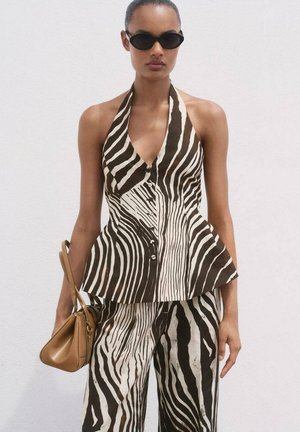 Brown and white striped peplum top with halter neck and button closure, paired with matching wide-leg pants. Brown handbag and dark sunglasses.