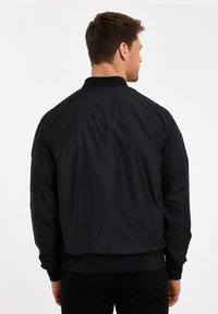 Schwarze Bomberjacke, glattes Nylonmaterial, gerippter Kragen und Bündchen, mit Reißverschluss versehene Taschen, lockere Passform, matte Textur, minimalistisches Design.