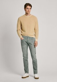 Bežani rebrasti pleteni pulover s okruglim izrezom, uparen s svijetlozelenim slim-fit trapericama. Cipele su bijele s smeškim đonovima.
