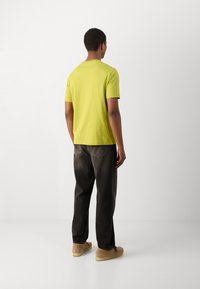 Lazdos žalios spalvos trumpa rankovė t-shirt, laisvas kirpimas, derinama su tamsiai rudi džinsais ir šviesiai rudais batais, matoma iš nugaros.