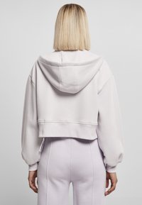 Lys grå cropped hettegenser med hette og senkede skuldre. Myk stoffkvalitet, ribbet kant, kombinert med lyse lilla bukser.