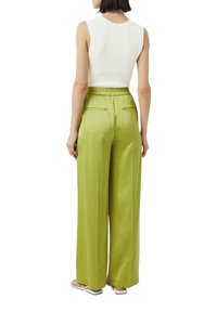 Biały, prążkowany, bezrękawnik w połączeniu z wysokim stanem, szerokimi spodniami w intensywnym zielonym satynie. Spodnie mają tylne kieszenie.