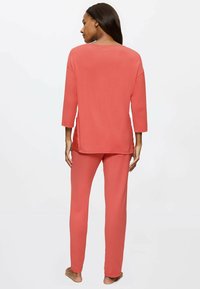 Ensemble de loungewear corail comprenant un haut ample à manches longues avec un col rond et un pantalon assorti. Tissu lisse au toucher doux.