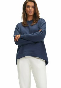 Navyblaue Sweatshirt, aus Baumwollmischung, entspannte Passform mit gerippten Bündchen und Saum. Kombiniert mit weißen Hosen und zeigt ein schlichtes, modernes Design.