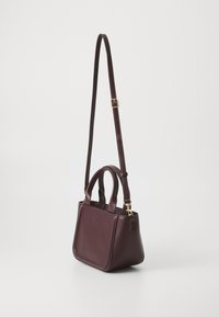 Piccola borsa in pelle bordeaux con doppio manico e tracolla staccabile. Texture liscia e design minimalista, con hardware in tonalità oro.