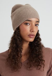 Bonnet en tricot beige avec une texture côtelée et une coupe ajustée. Matière douce et chaude avec un léger affaissement au sommet.