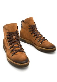 Beżowe zamszowe botki za kostkę z ciemnobrązowymi sznurowadłami, okrągłymi noskami i kontrastującymi ciemnimi gumowymi podeszwami. Złote akcenty na oczkach do sznurowania.