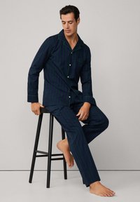Conjunto de pijama azul marino con rayas verticales verdes y moradas, que incluye una camisa con botones y un bolsillo, y pantalones a juego. Tejido suave.