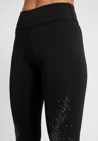 Svarta leggings med hög midja, tillverkade av stretchtyg, med en gradiente av små vita till silverfärgade prickar nära fållen.