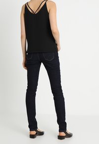 Top negro sin mangas con cuello en V y diseño de doble tira, combinado con jeans ajustados de mezclilla azul oscuro y zapatos planos negros. Look limpio y sencillo.