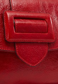 Sac à main en cuir rouge avec une finition texturée. Il présente un rabat rectangulaire avec une fermeture surélevée et des coutures contrastantes.