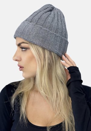 Grå ribbet strik hue med en foldet skygge. Teksturen ser blød ud og har lodrette striber. Stylet på en model med blond hår.