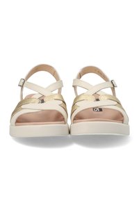 Sandalias en crema y oro con correas cruzadas, un empeine texturizado y una suela de goma blanca baja. Presentan una hebilla en la correa del tobillo.