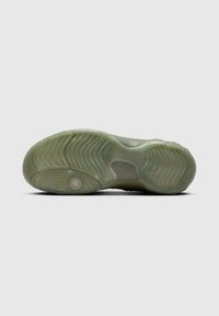 Suela de una zapatilla deportiva de goma verde claro con un patrón de banda de rodadura ondulado y detalles de amortiguación visibles sobre un fondo gris liso.