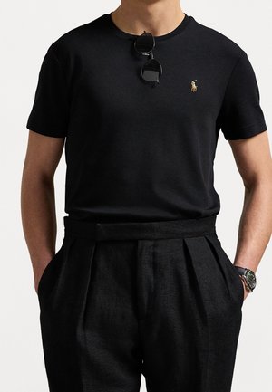 Czarna bawełniana koszulka z krótkim rękawem i małym haftowanym logo. Zestawiona z czarnymi spodniami w kant o wysokim stanie oraz zegarkiem.