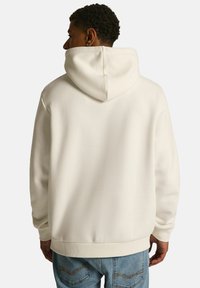 Biała bluza z kapturem o miękkiej fakturze, z prążkowanymi mankietami i hemem. Tył ma prosty, czysty design bez logo.