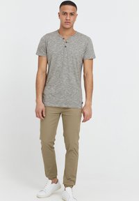 Grå kortärmad henley t-shirt med tre knappar, matchad med beige tapered byxor och vita sneakers, visad mot en vit bakgrund.