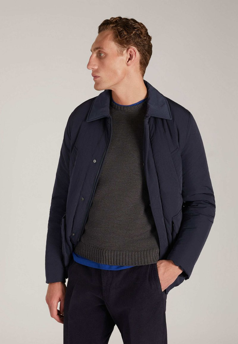 Doudoune marine avec un design à col, associée à un pull en tricot charbon. Dotée d'une fermeture éclair et d'un tissu texturé.