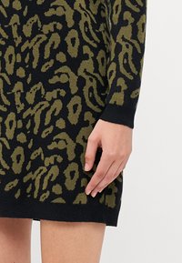 Strikket kjole med svart base og grønn leopardtrykk, ribbede mansjetter og en tettsittende silhuett. Glatt tekstur med lengde til midten av låret.