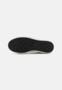 Svart gummiyttersåle med et teksturert mønster, med diamantformer og en logo, kantet av en hvit mellomsåle. Klassisk sneakersdesign.
