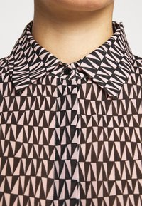 Gros plan d'un col de chemise boutonné avec un motif triangulaire géométrique noir et rose clair.
