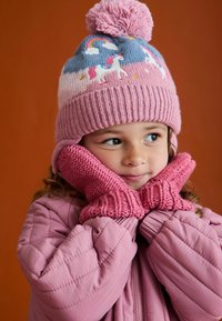 Miękka różowa dzianinowa czapka z pomponem i haftem w kształcie jednorożca, w zestawie z dopasowanymi różowymi dzianinowymi rękawiczkami i puszystą różową kurtką.