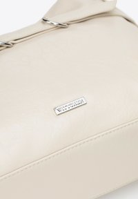 Borsa in pelle color crema con una texture liscia, dotata di una placca del logo argentata e un rilascio pieghevole sicuro con hardware in metallo.