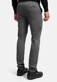 Pantalon gris texturé au design ajusté, avec des poches arrière à fermeture à bouton et des chaussures sombres assorties.
