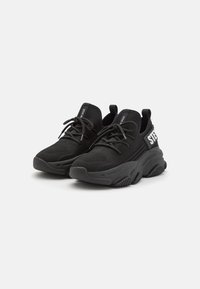Zapatillas deportivas negras con parte superior de malla texturizada, suela de goma, cierre de cordones y un acento de logo en el lateral. Punta redondeada y talón acolchado.