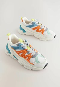 Białe sneakersy z pomarańczowymi, niebieskimi i szarymi akcentami. Materiał siateczkowy z masywną podeszwą, teksturowymi nakładkami i odblaskowymi sznurówkami. Neonowe żółte detale.