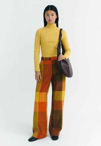 Mustard ribbed turtleneck, multicolored checkered high-waisted wide-leg pants in orange, yellow, and brown. Black shoulder bag, black shoes.