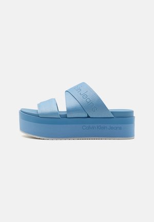 Blaue Plateausandale mit zwei Stoffriemen und "Calvin Klein Jeans"-Markierung an der Seite und am oberen Riemen, seitlich dargestellt.