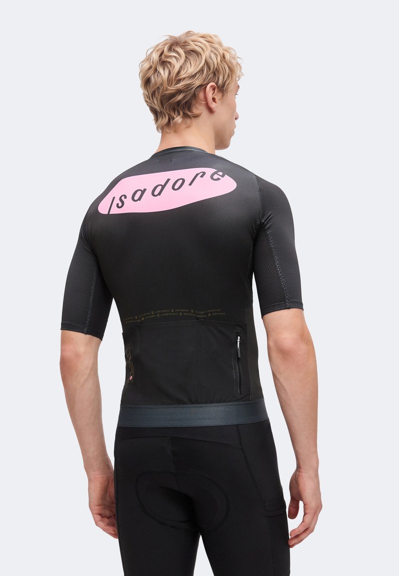 Homme blond portant un maillot de cyclisme noir avec un logo rose "Isadore" sur le haut du dos, dos tourné, les mains détendues le long du corps.