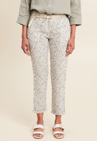 Lichtgroene geprinte broek met een lovertjespatroon, cropped lengte, en een gevlochten lichtbeige riem. Gecombineerd met witte sandalen.