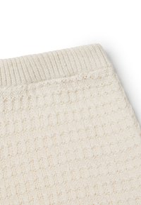 Tessuto lavorato a maglia color crema con un motivo testurizzato, caratterizzato da polsini a coste e un aspetto morbido e leggero.