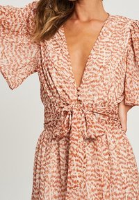 Kukallinen kietaisumekko pehmeässä oranssissa ja valkoisessa. V-pääntie, jossa on solmittava vyötärö ja väljät, leijailevat hihat. Kevyt kangas.