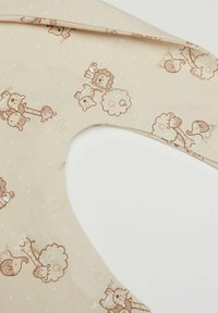 Béžový látkový bryndák s potiskem světle hnědých zvířat, včetně lvů, slonů a ovcí, malými bílými tečkami a zaklapávacími uzávěry.