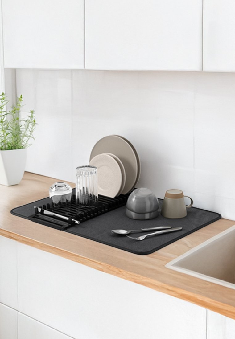 Grau Abtropfmatte auf einer Holztheke mit verschiedenen Geschirr: zwei braune Teller, ein Glas und zwei graue Tassen sowie silbernes Besteck.