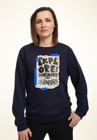 Granatowy sweter z długimi rękawami, ozdobiony teksturowanym naszywką z napisem "ZBADAJ! TROCHĘ WIĘCEJ PRZYGODY" w wyraźnym czarnym kroju.