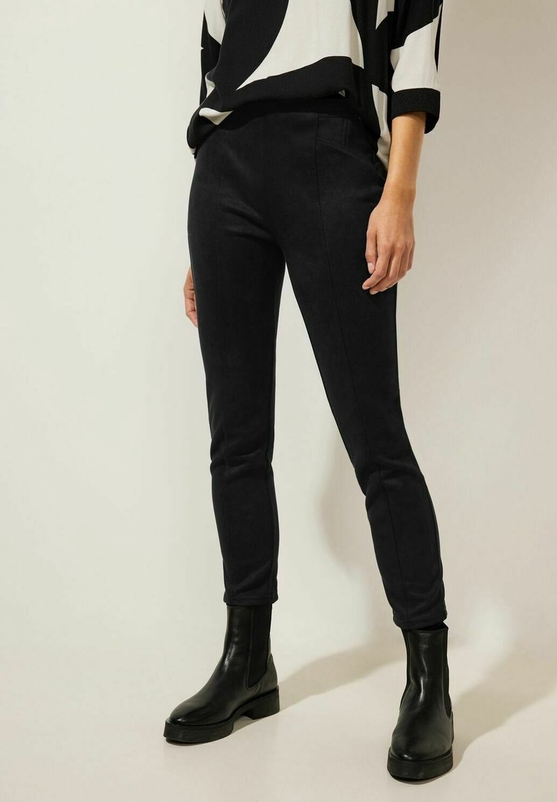 Pantaloni neri aderenti realizzati in tessuto morbido, caratterizzati da una texture liscia e un design slim. Abbinati a stivali neri alla caviglia per un look elegante.