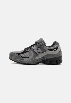 Graue Laufschuhe mit einer Kombination aus Wildleder und Mesh-Materialien, einer runden Zehenpartie, gepolstertem Kragen und einer dicken, schwarzen Gummisohle mit Rillen.