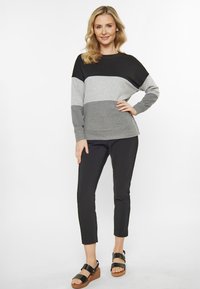 Felpa a maniche lunghe in blocchi di colore nero, grigio chiaro e grigio scuro, abbinata a pantaloni neri aderenti e sandali neri con plateau.