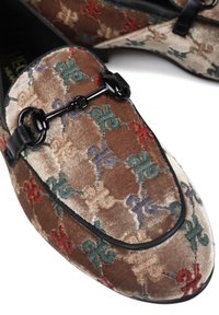 Aksamitne mokasyny z wielokolorowymi haftowanymi wzorami fleur-de-lis oraz czarnym metalowym detalem w kształcie wędzidła na górnej części.