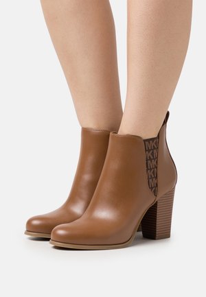 Hnědé kožené kotníkové boty s kulatou špičkou, texturovaným širokým podpatkem a hnědým elastickým bočním panelem s vzorem a logem.