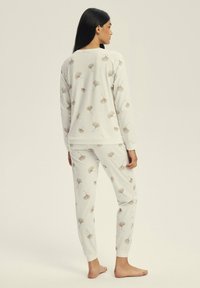 Pajama set in light gray fabric featuring a repeated ginkgo leaf pattern in beige. Long-sleeve top and fitted pants with cuffed ankles.