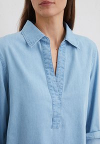 Lichte blauwe, gecollumeerde shirt met een placket halslijn en lange mouwen. Gemaakt van zachte, lichte stof met een gladde textuur.